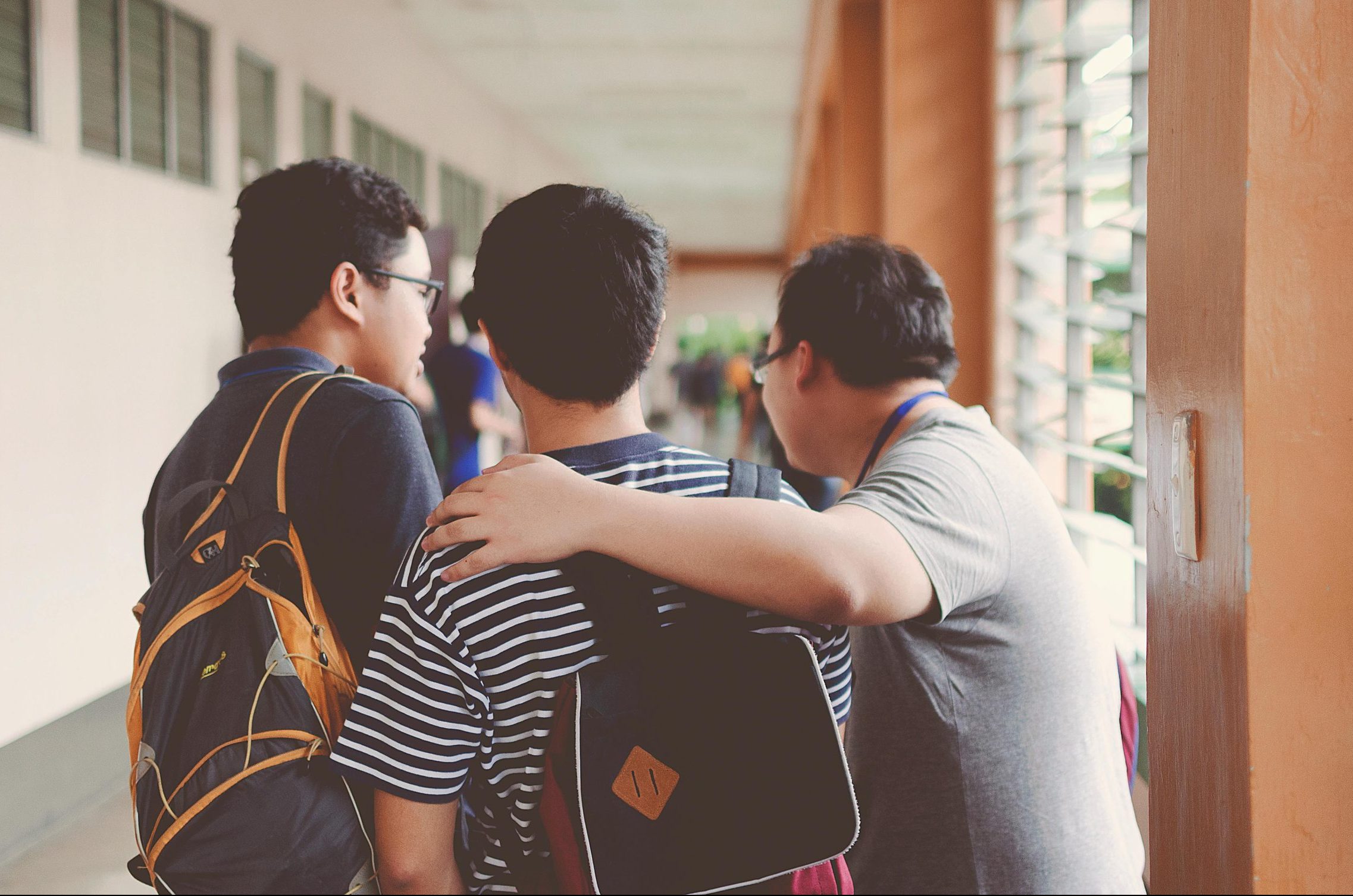 Picture showcasing the backs of three young men. One has their arm around the other to show support and caring behaviour.